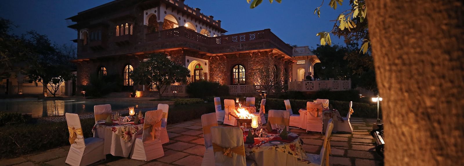 An outdoor dining area set under a tree, beautifully lit for a serene evening meal - Khas Bagh, Jaipur.
