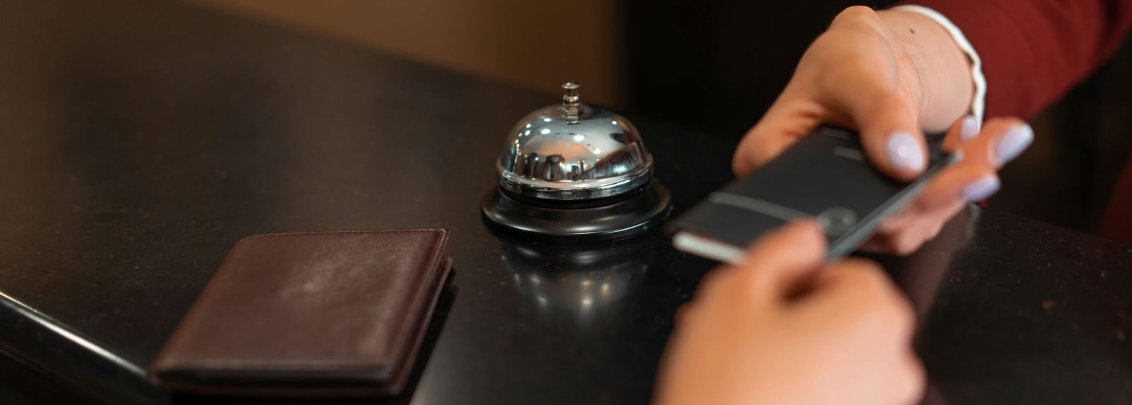 A hand giving and another hand holding onto a small note over the reception desk, with a bell to the side.