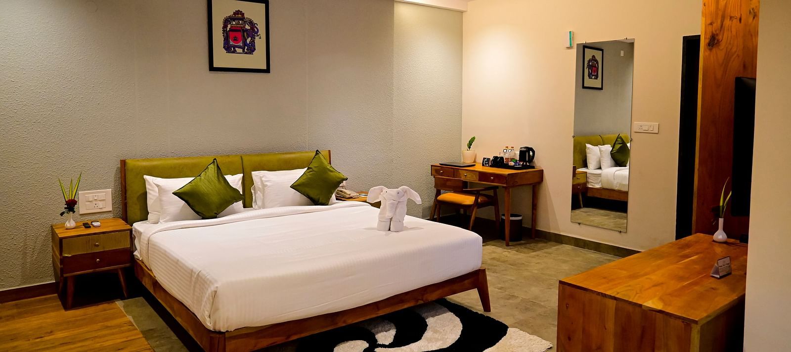 Hotel room with a large bed, olive green pillows, a unique black and white rug, and wooden furniture at TGI Livancia Hillside, JC Nagar, Mysore
