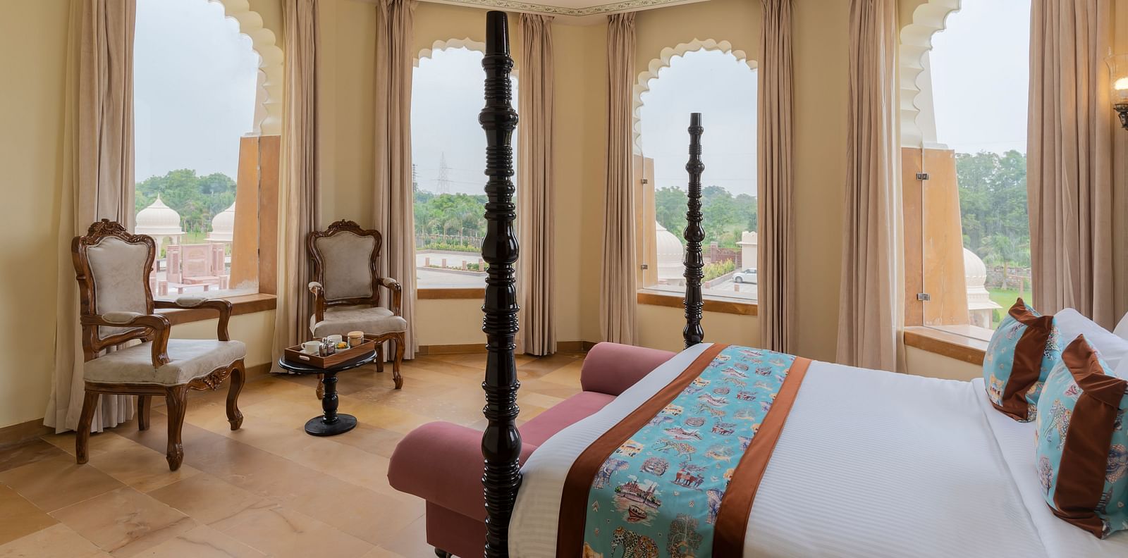 Elegant bedroom with arched windows overlooking scenic landscape at Kesar Bagh Palace.