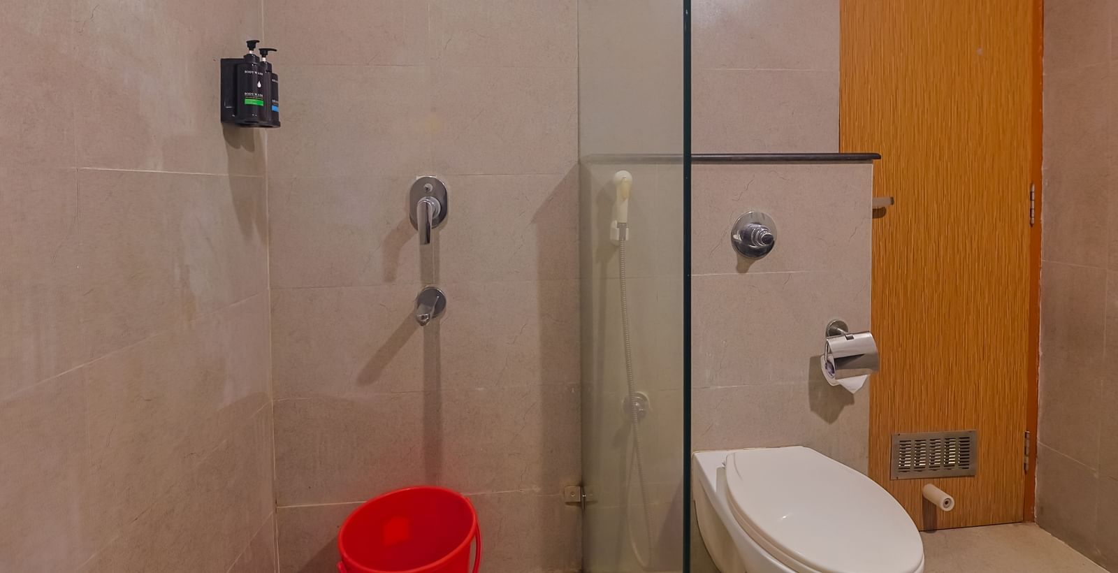 Bathroom with toilet, shower area and glass partition at Max Hotel Prayagraj.