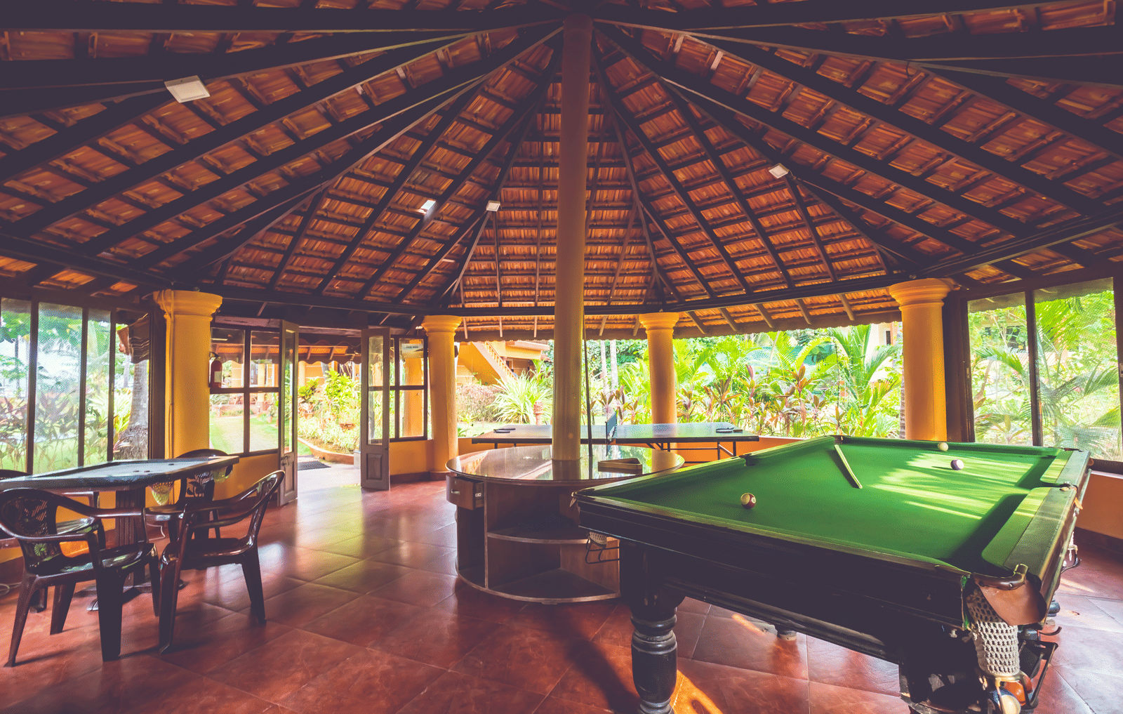 Open-sided hut with a tiled roof, containing a green snooker table and wooden seating at Paradise Lagoon Resort, Udupi.