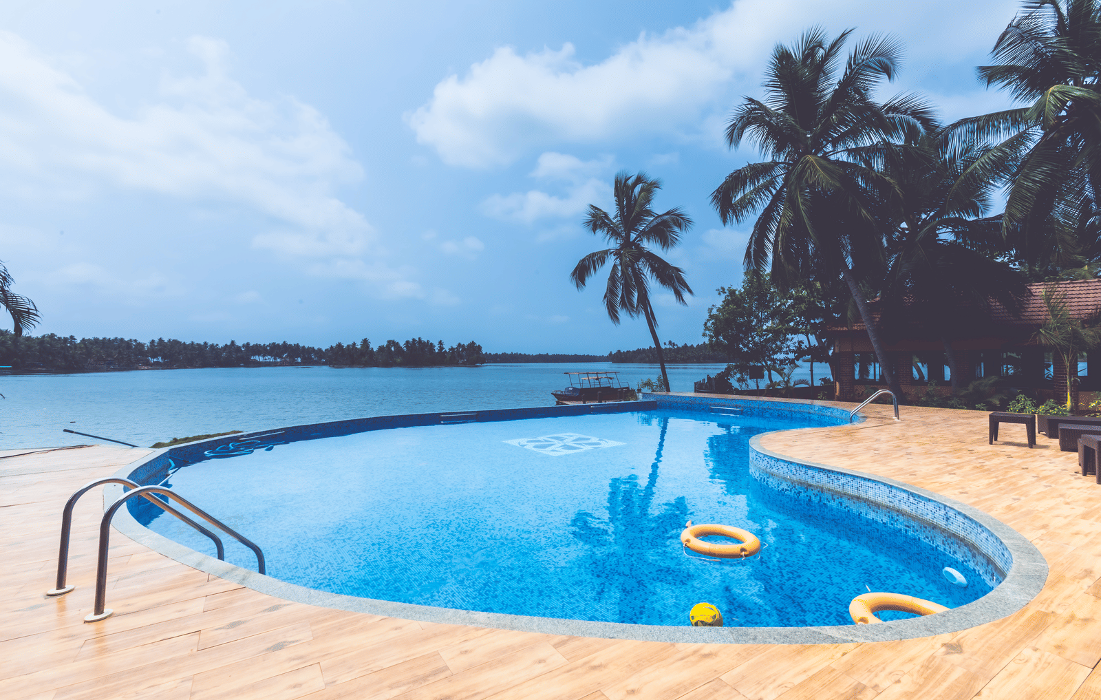 Swimming pool with pool floats, surrounded by palm trees and open sky at Paradise lagoon Resort, Udupi.