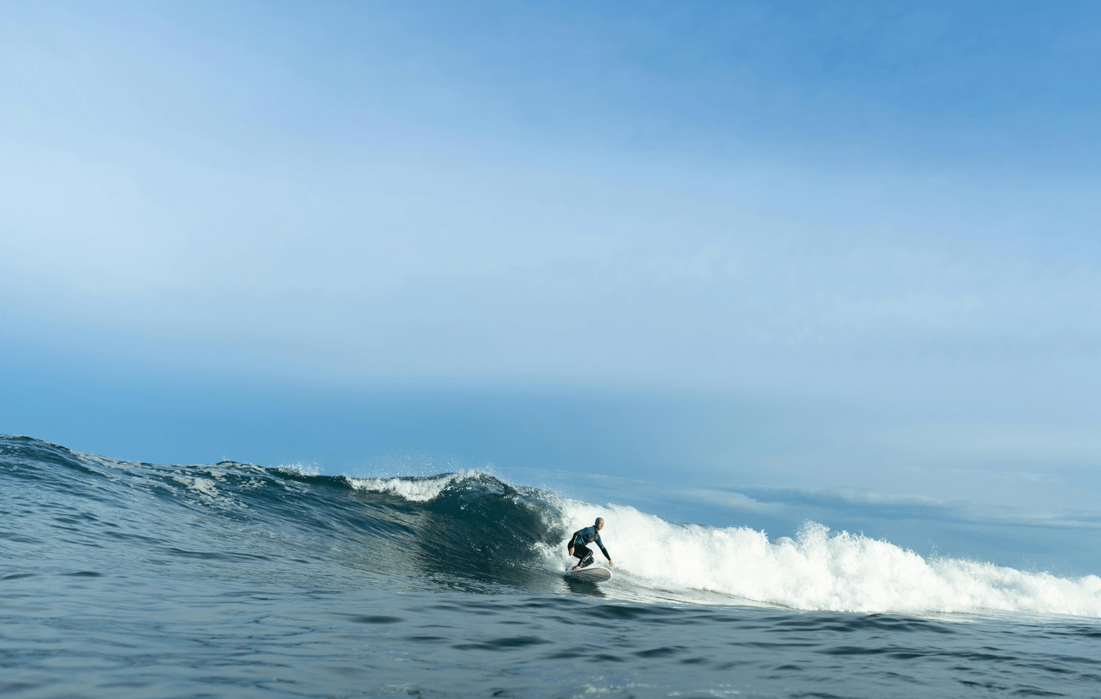 Surfer riding a wave in the ocean with blue water and clear sky in the background.