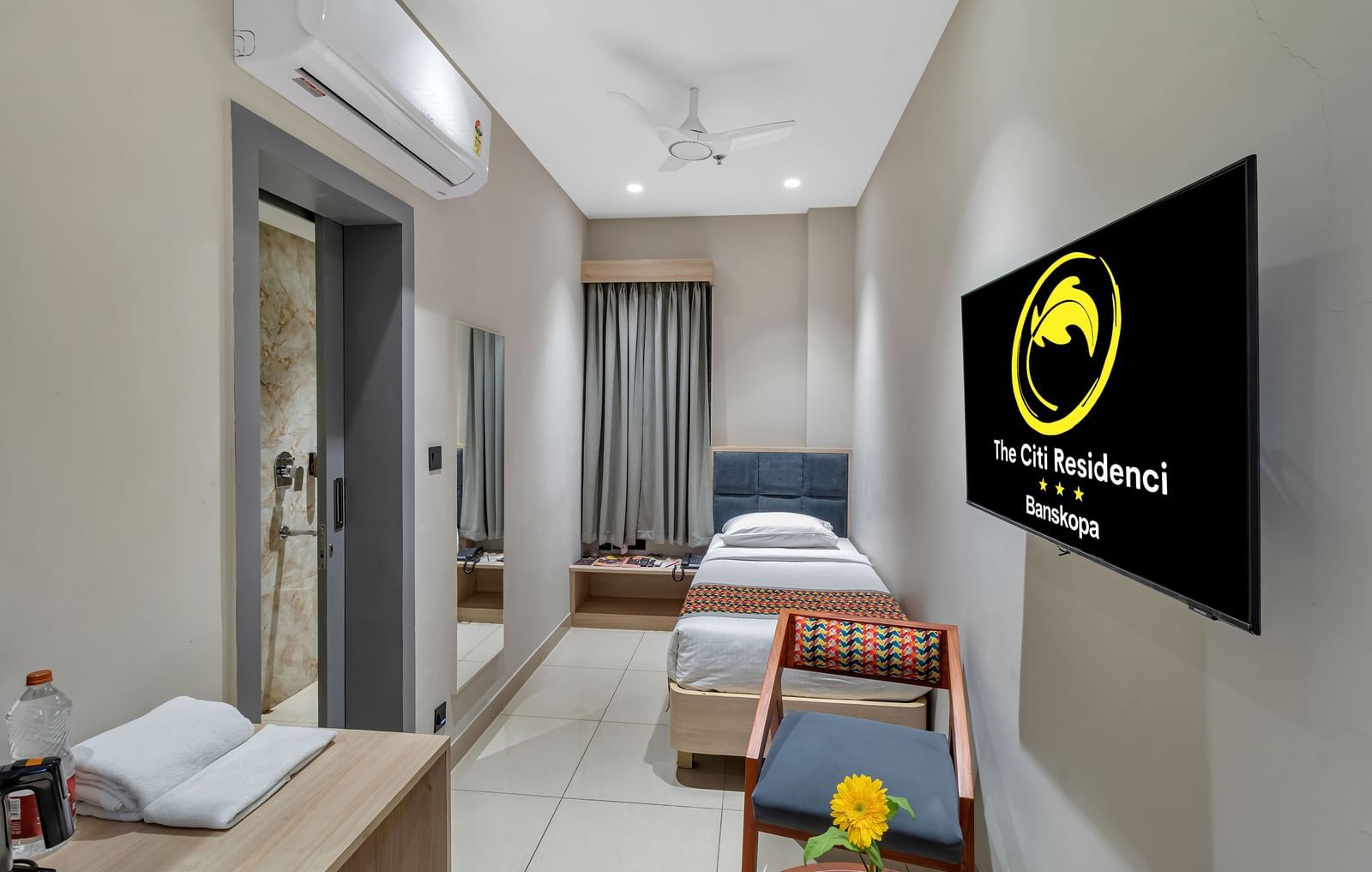 A compact hotel room with a single bed, a chair, a desk, and a wall-mounted television | The Citi Residenci Hotel Banskopa