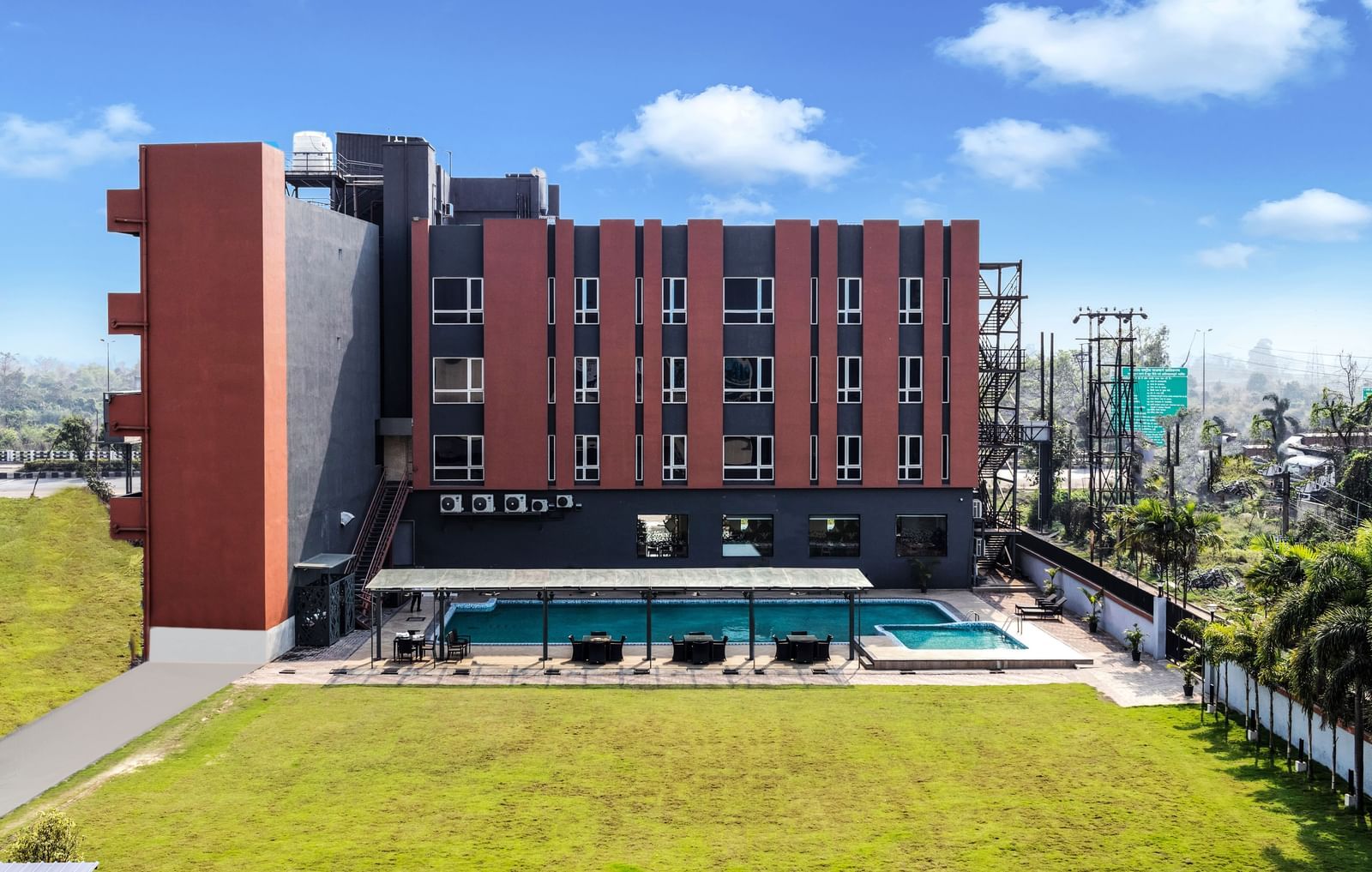 A modern hotel building with a swimming pool and green lawn under a partly cloudy sky | The Citi Residenci Hotel Banskopa