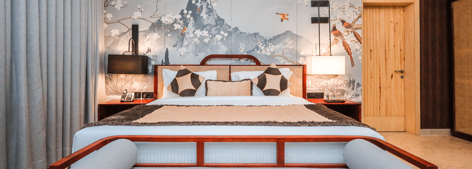 4. Bed Frame A room shows a bed with a large cushioned frame, side tables, artwork above the bed and curtains on a window at Ananta Spa & Resort, Jaipur.