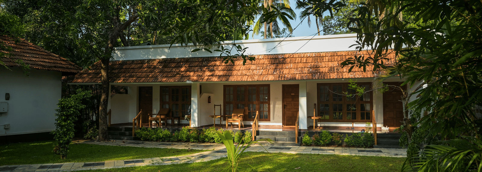 A guest villa with tiled roof overlooking a lush, sunlit lawn at Ayur On The Beach Nattika.