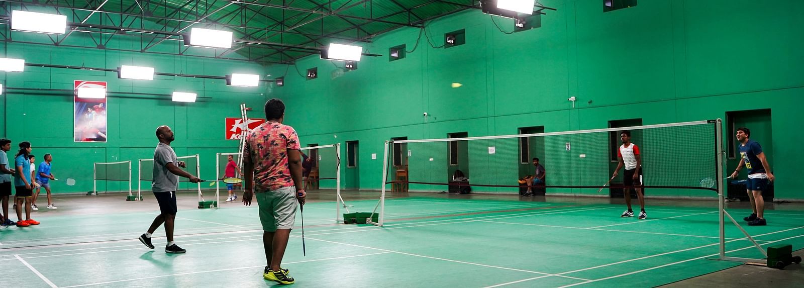 An indoor badminton court at BNGV Grandeur Hotel and Banquets, with green flooring and a few people playing.