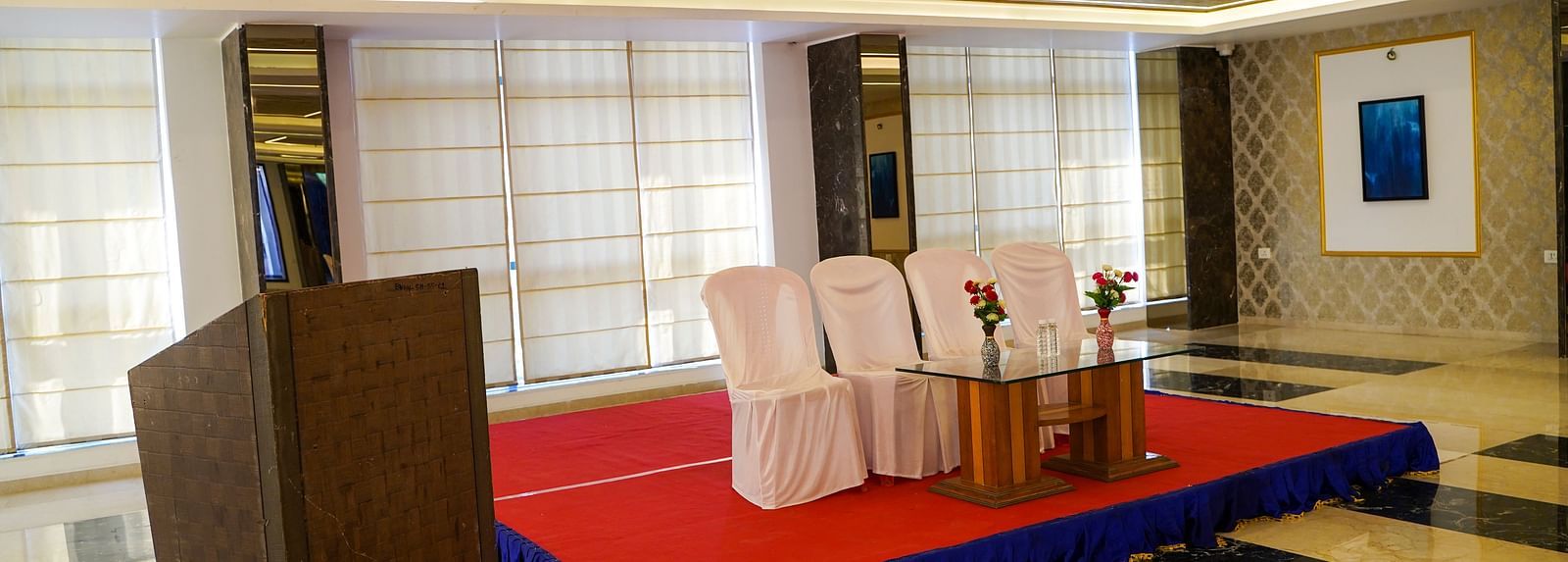 A well-lit smaller space at BNGV Grandeur Hotel and Banquets, arranged for an event with tables, chairs, and a podium.
