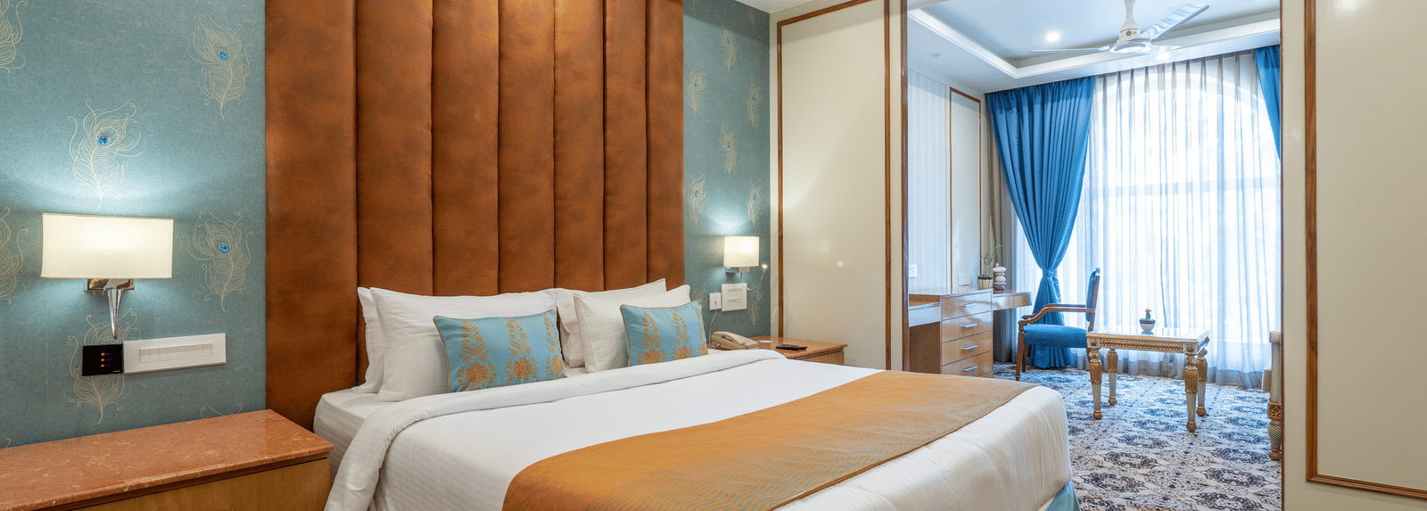 Wide shot of a contemporary hotel room with a spacious bed, nightstands, and a teal and terracotta colour scheme at Hotel Hukam's Lalit Mahal.