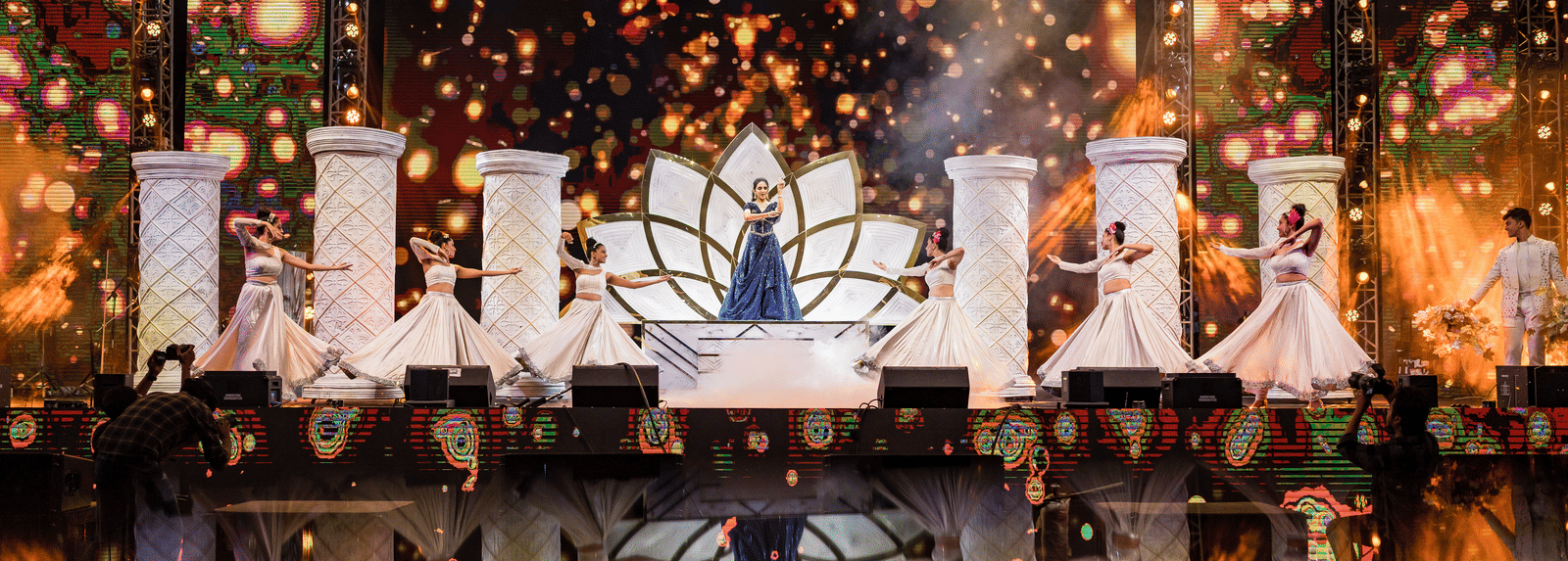 A dark stage background with glowing, ornate decor elements and intense warm stage lighting and sparkling effects at Hotel Hukam's Lalit Mahal.