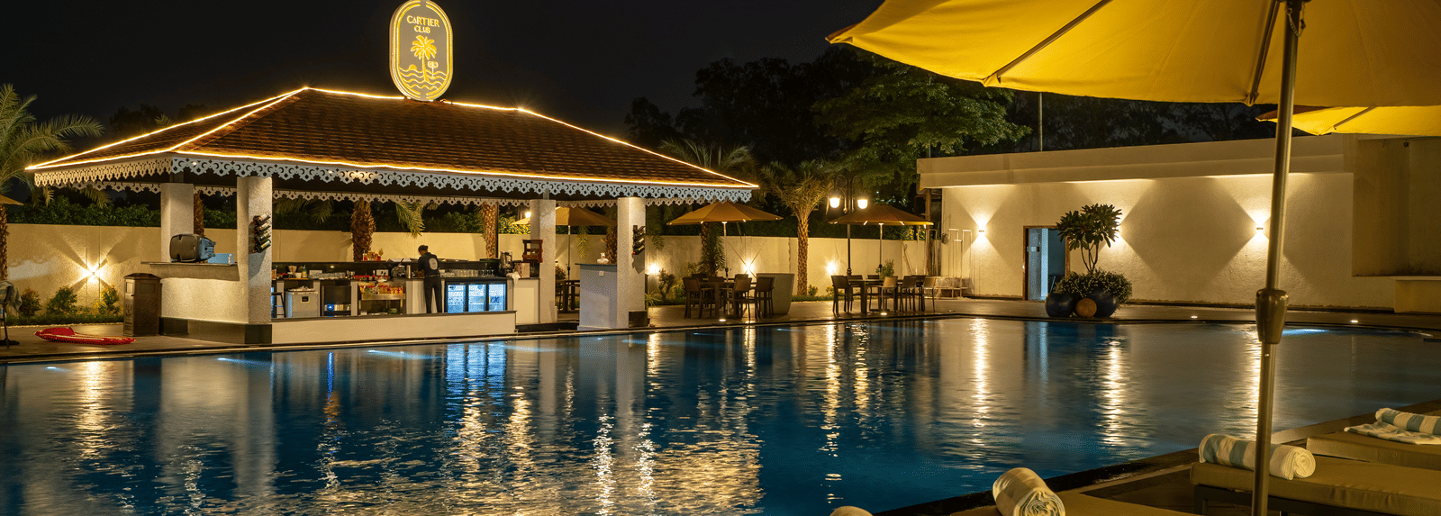 Evening view of the swim-up bar area next to the pool, featuring seating and ambient lighting under an umbrella at Hotel Hukam's Lalit Mahal.