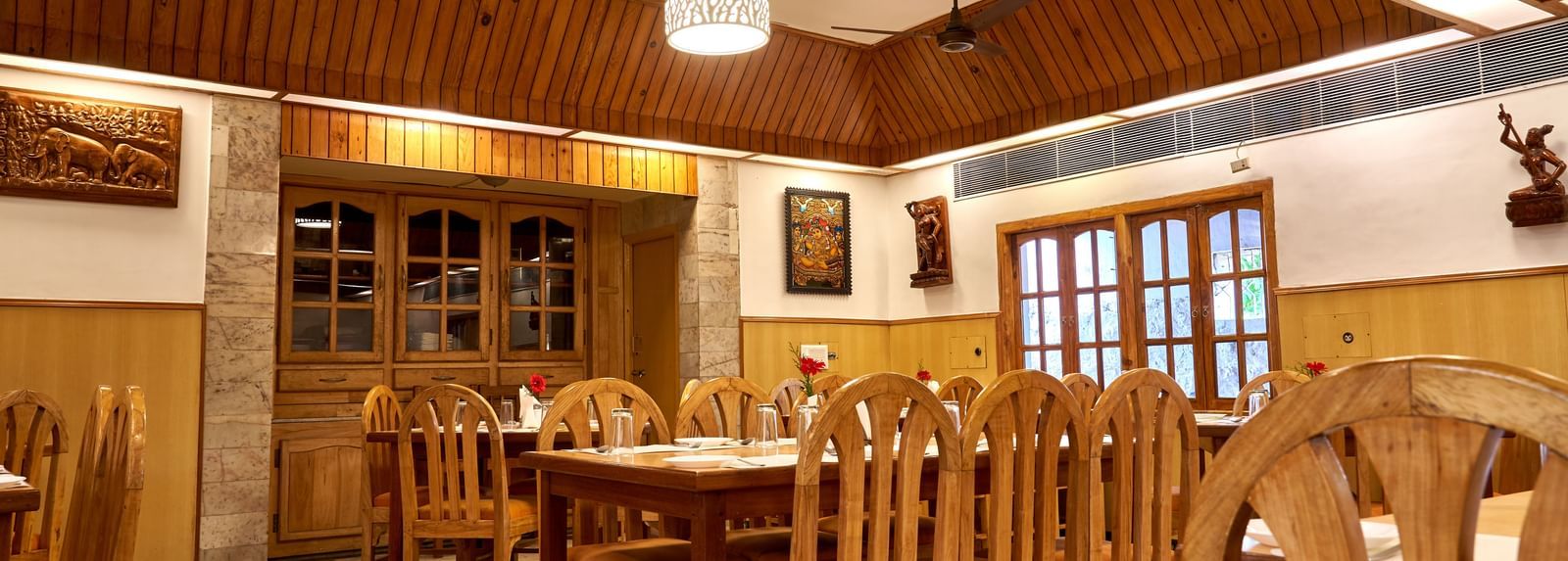 Another view of the restaurant at Hotel Mamallaa Heritage, showcasing multiple wooden dining sets and a distinctive patterned wooden ceiling.