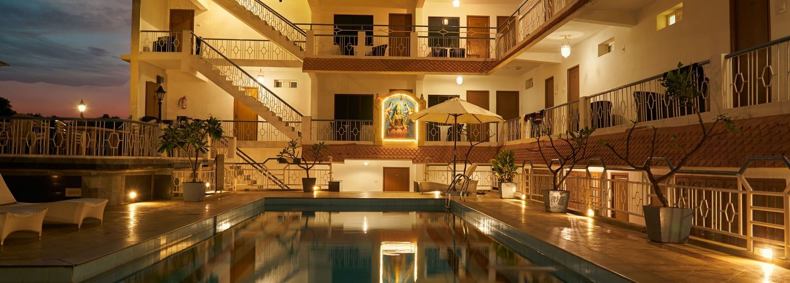 A nighttime view of Hotel Mamallaa Heritage, showcasing its illuminated facade and a beautifully lit swimming pool reflecting the lights.