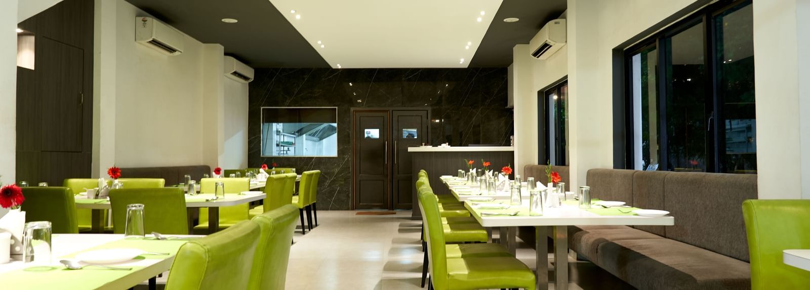 A modern restaurant interior at Hotel Mamallaa Heritage, characterized by bright lighting, white walls, and tables with vibrant lime green seating.