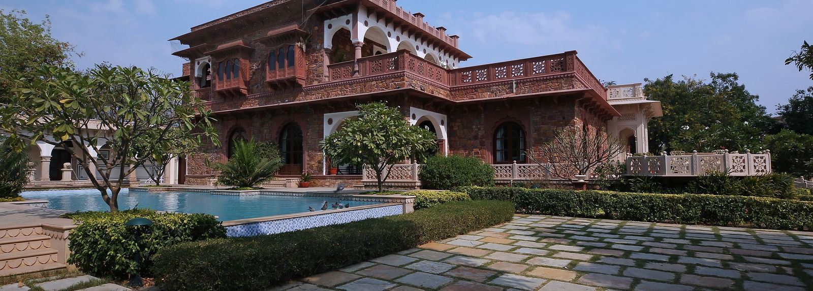 A majestic heritage palace with a cobblestone pathway, bushes and lush greenery in the backdrop - Khas Bagh, Jaipur.