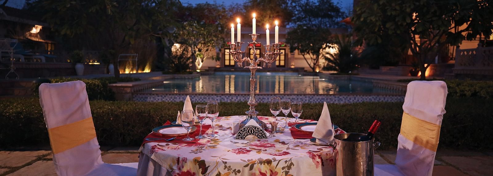 A beautifully set outdoor dining table illuminated at dusk, with buildings in the background - Khas Bagh, Jaipur.
