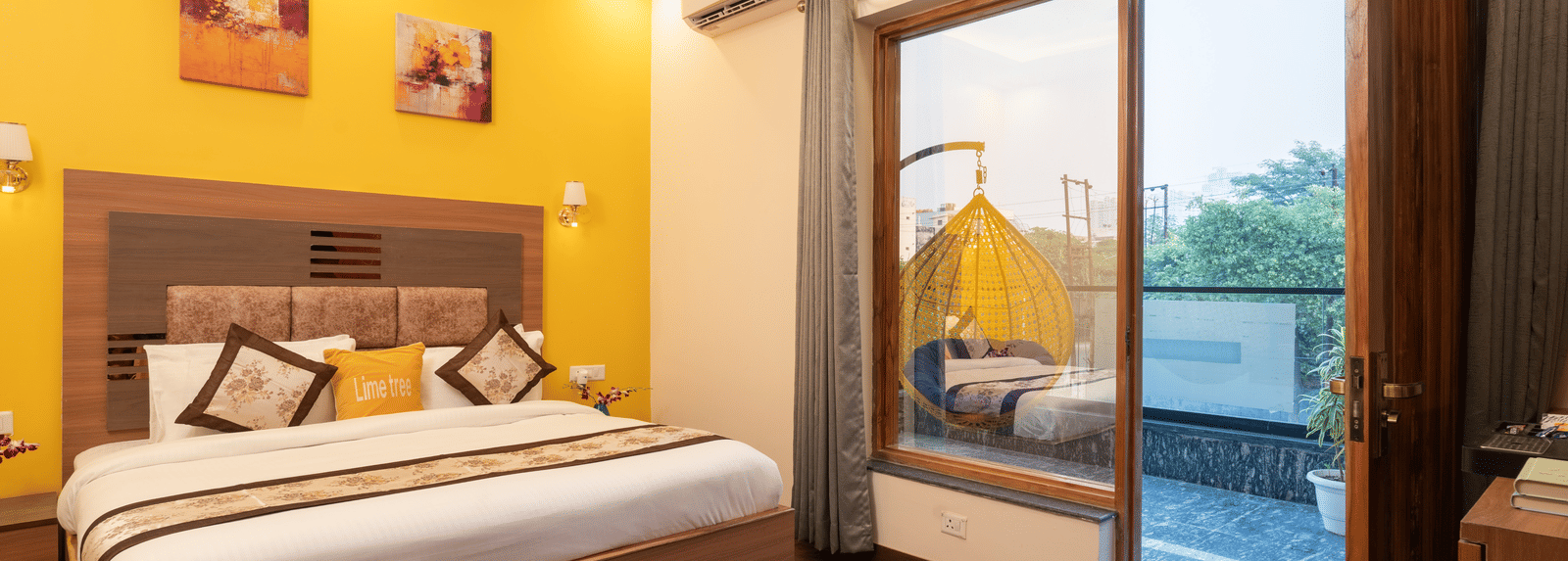 An image of a bedroom with a double size bed, a bedside table, and a glass slider door leading to the balcony - Lime Tree Hotel & One BHK, Noida Sector 50