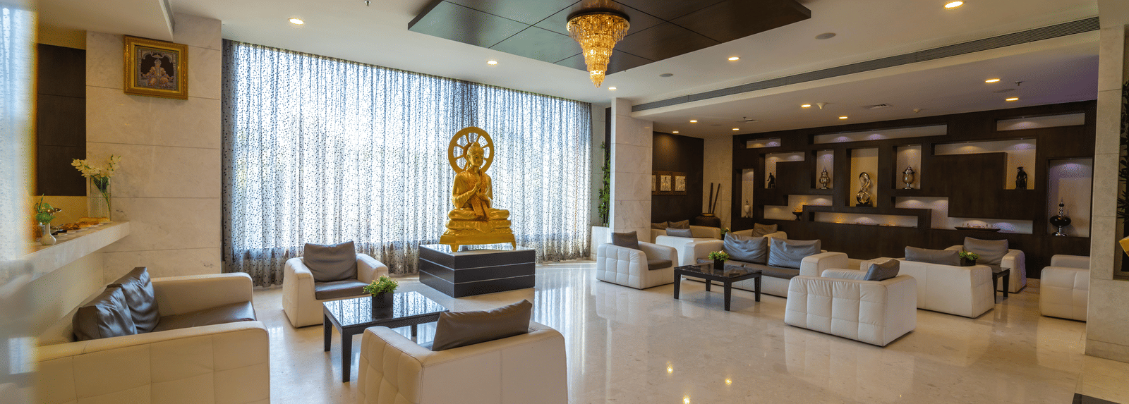 Hotel lobby area with amble seating and warm lighting, and a statue of an idol in the centre at Narayani Heights Hotel & Resorts, Ahmedabad.