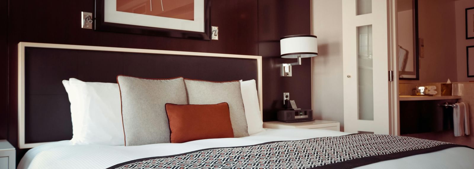 A hotel bedroom with a large bed, crisp white linen, and a cushioned headboard.