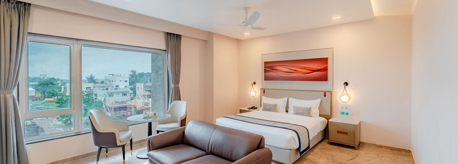  A spacious room with a king-size bed, a sofa, and a city view | Studio Suite | Pravasa Hotel, Vijayapura