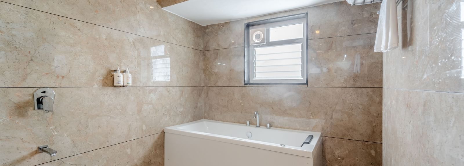 A suite bathroom with a white bathtub and patterned beige tiles | Suite | Pravasa Hotel, Vijayapura