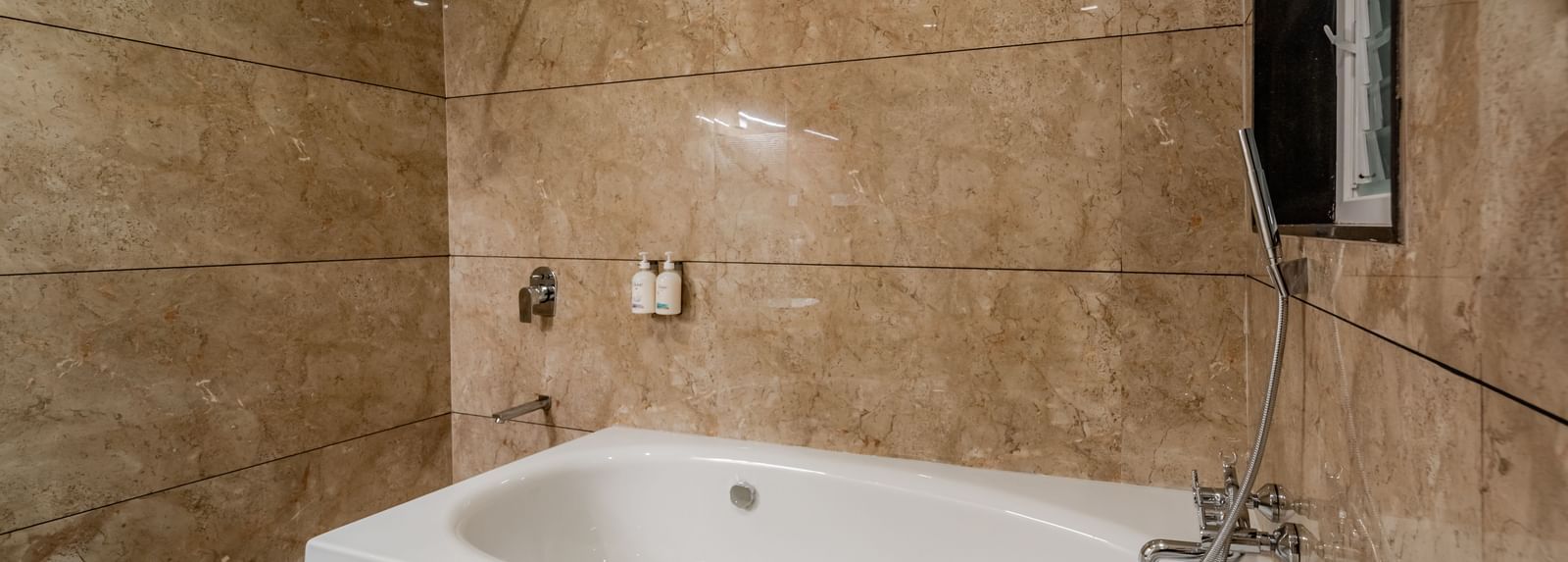 Modern bathroom with a clean white bathtub and marble-patterned tiles | Premium Room | Pravasa Hotel, Vijayapura