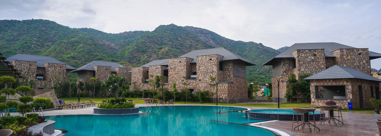 A swimming pool reflects the resort buildings. The surrounding area has view of several holiday villas with a view of the mountains.