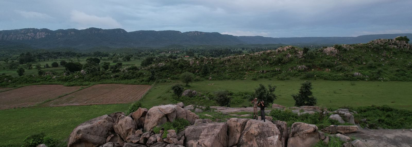 Two People standing on a rocky outcrop, holding binoculars.