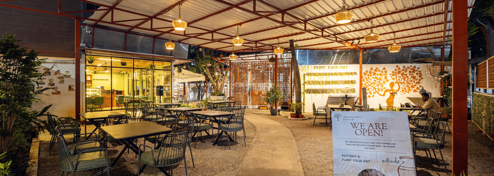 Claysutra Cafe & Restaurant at Kove Smart Stays seen during a darker time of the day, with ambient lighting, outdoor seating, and an overhead shed.
