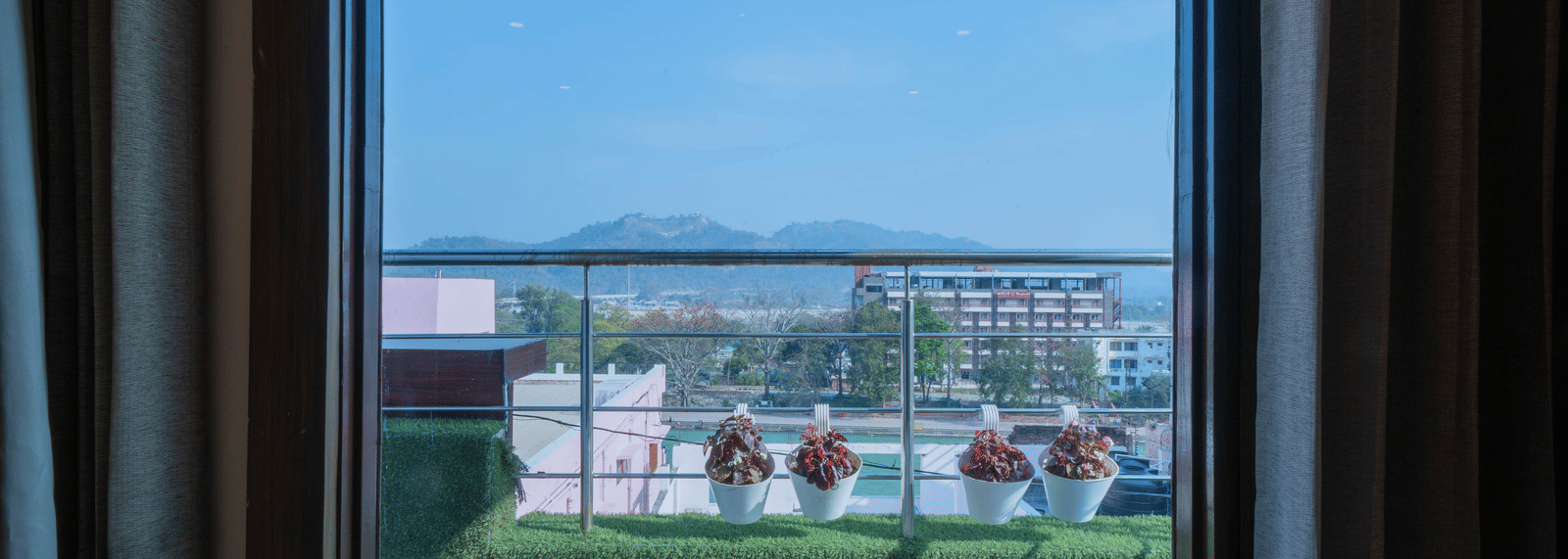 View from a hotel window overlooking a green outdoor terrace area and distant landscape - Perfectstayz Premium at Har Ki Pauri Road (Ganga Heights)