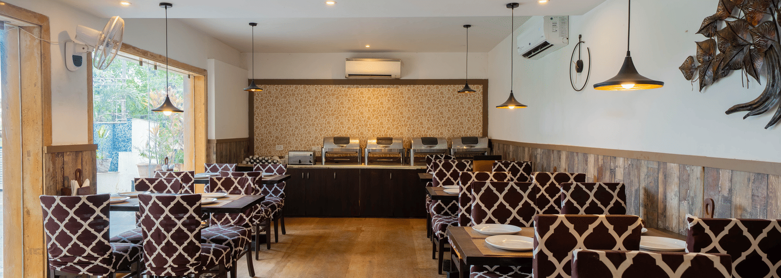 A well-lit, modern dining room featuring a patterned booth seating and wooden flooring at Perfectstayz Premium Goa Continental.