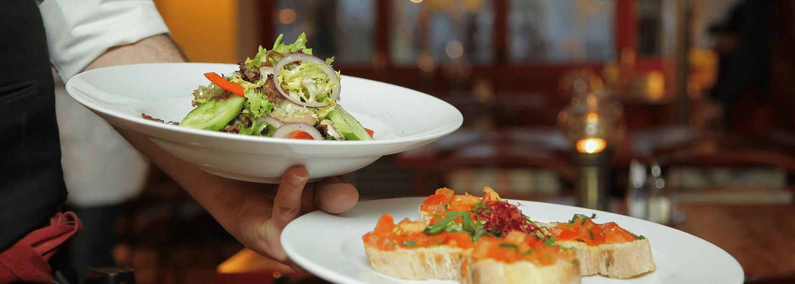 a person in a restaurant holding two plates with delicious cuisines in it that are well plated