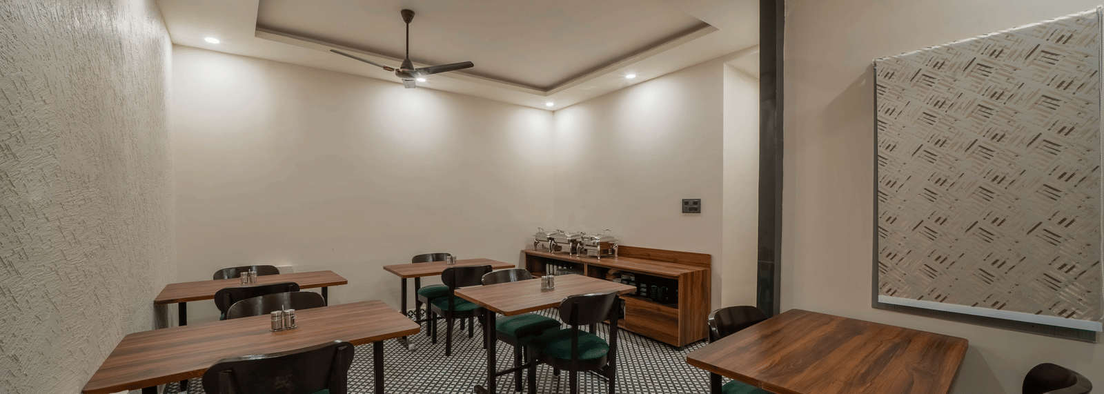 Side view of a dining room with dark wooden tables, chairs, and ceiling fans - Perfectstayz Value Aalaya Suites, Haridwar