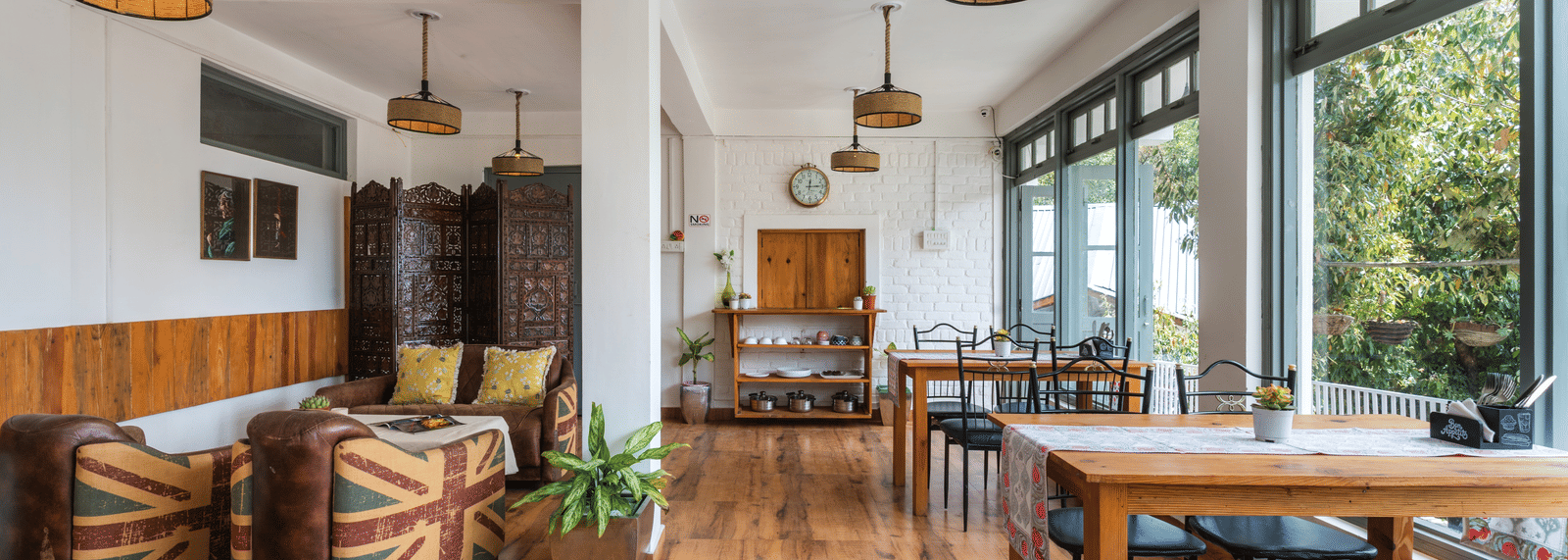 A close-up shot of Ziran Retreat's dining area, featuring a long wooden table with benches, and a small sitting area with striped armchairs, located near large windows.