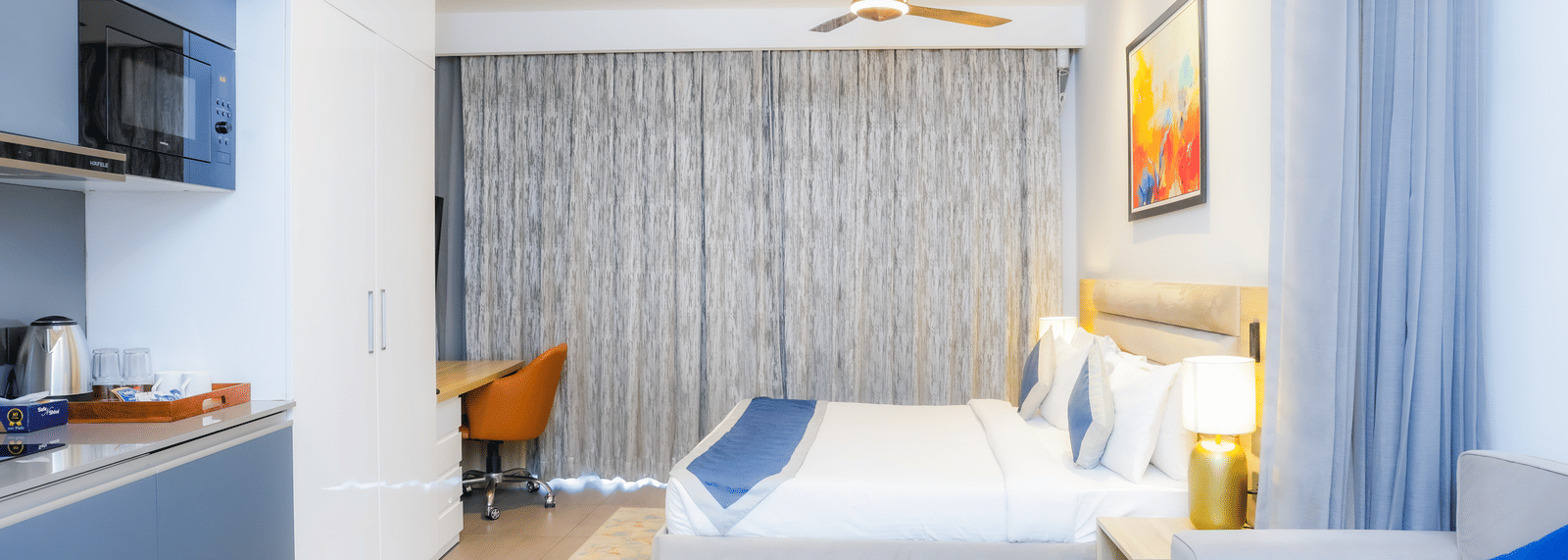 Contemporary bedroom with king size bed and blue curtains at Livbox Supernova, Noida.