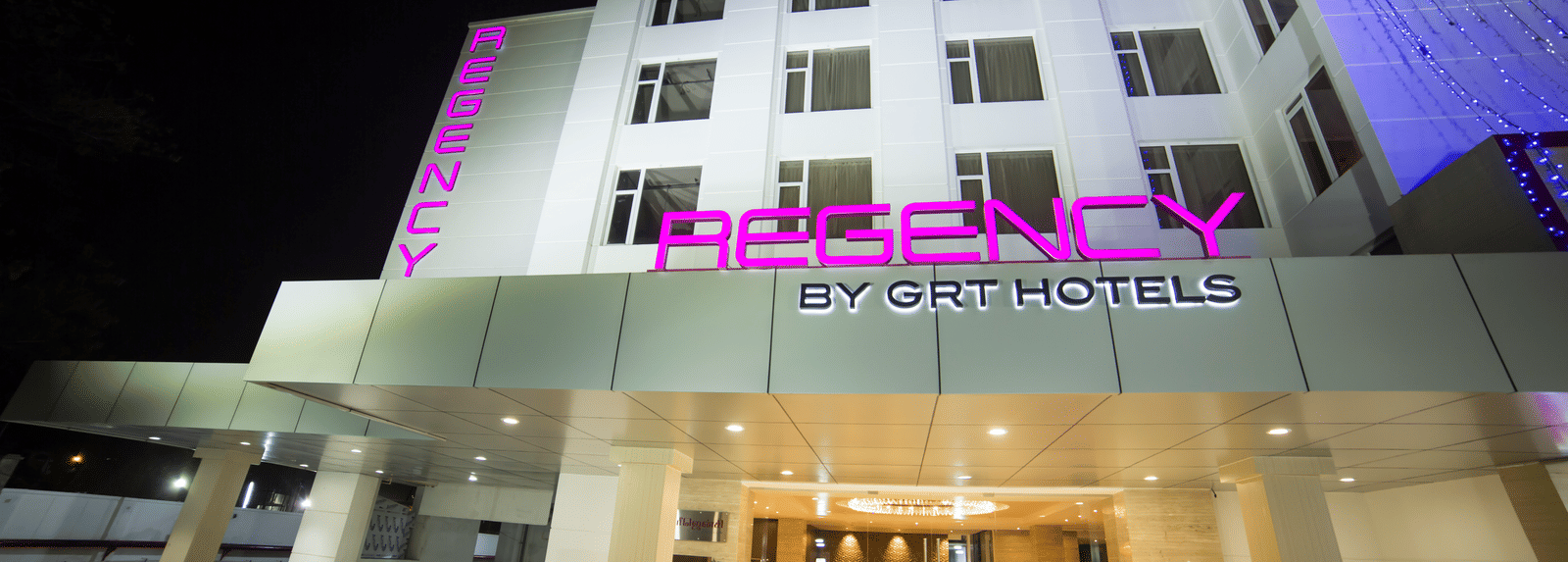 Regency GRT Hotels sign with purple letters and blue lights at night.