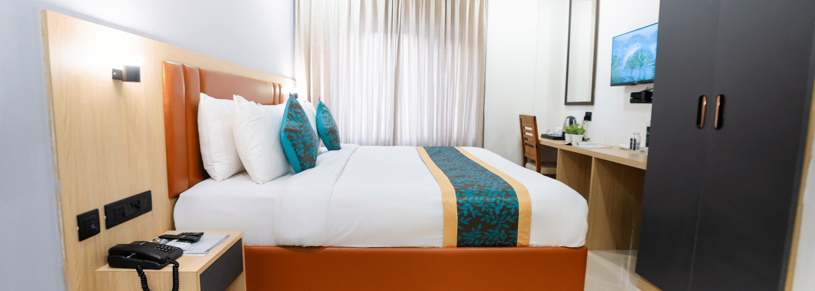 A room with a bed, cabinets, a wall-mounted television, and a side table at Sunrise Business Hotel, Hyderabad.