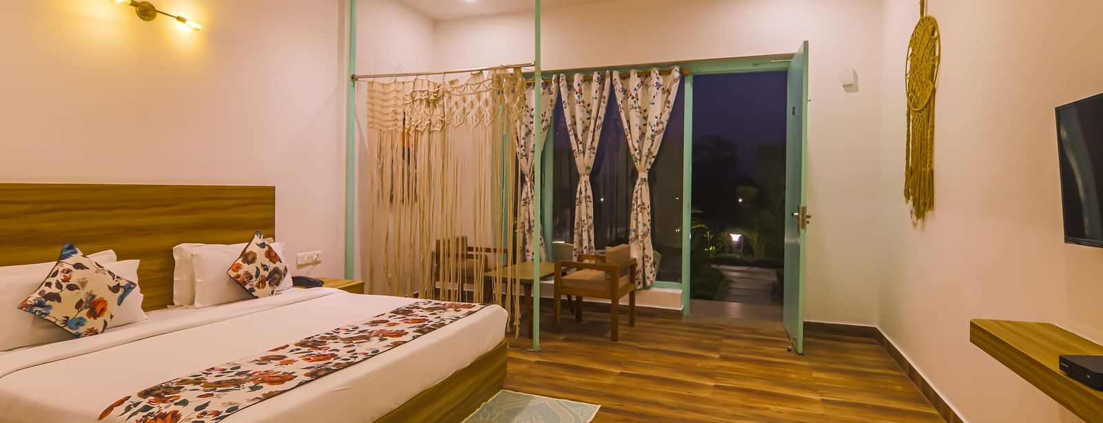 A well-lit bedroom at Vedikant Resorts The Mallard Corbett features a bed, seating area, and open balcony doors.