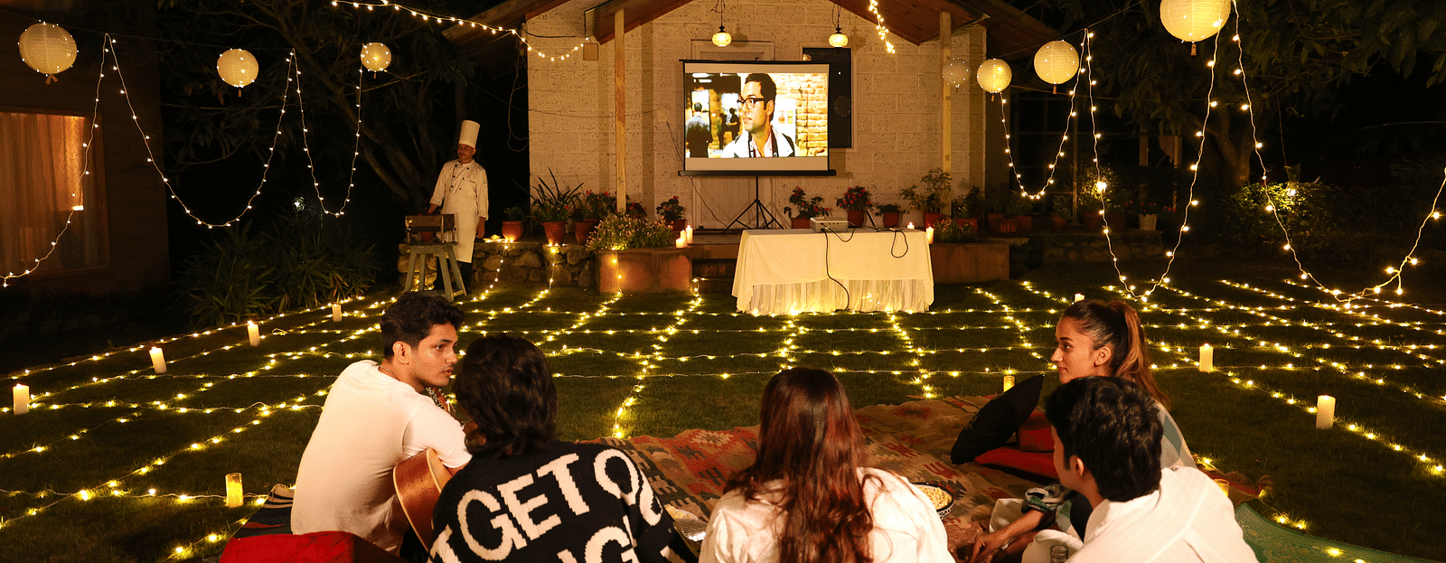 People enjoying an open movie night setup with lights and a projector set up at The Sylvan Retreat, Dehradun. 