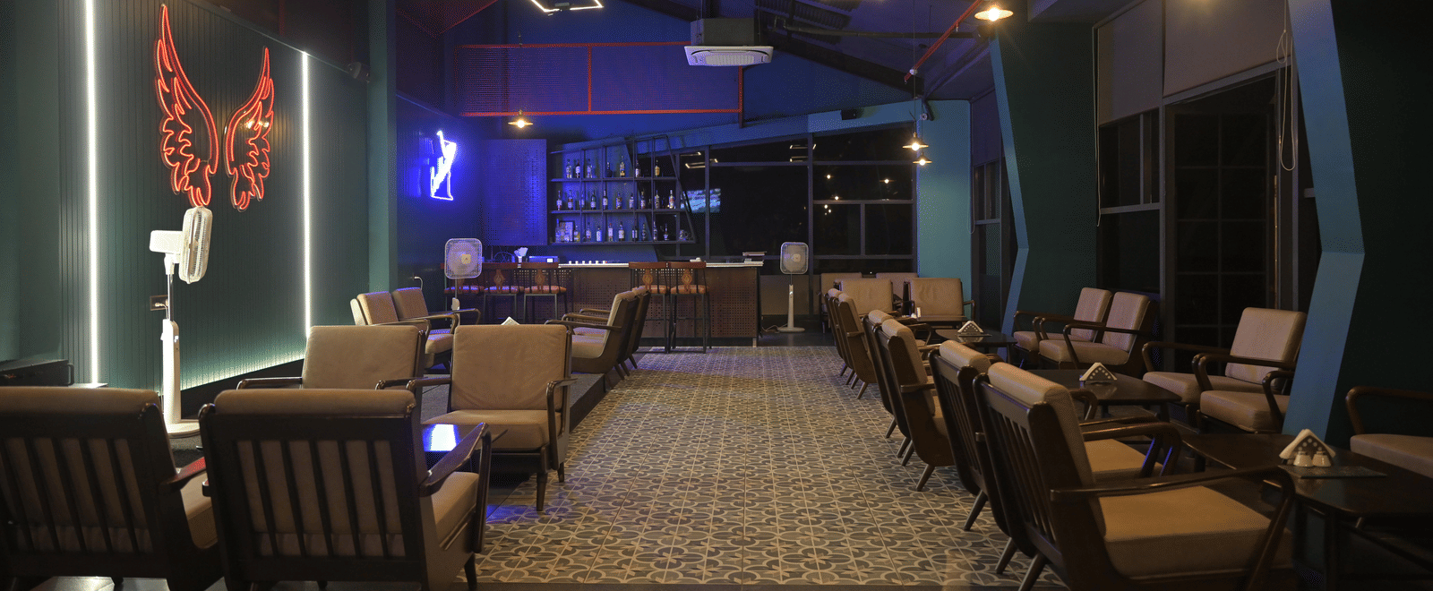 A wide evening view of the lounge bar with warm seating, patterned flooring, and soft neon lighting at Hotel Sonar Bangla Mayapur.