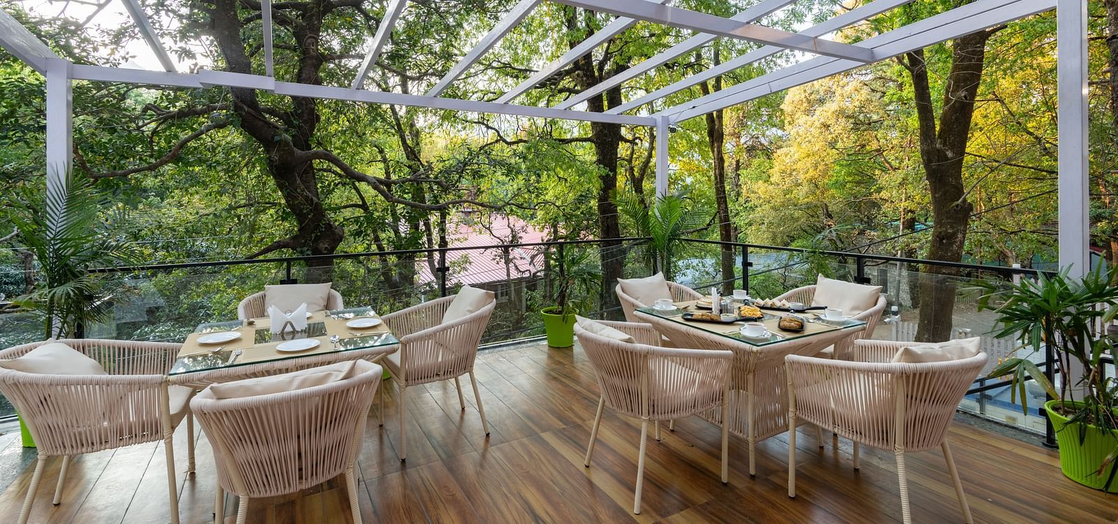 The deck at DLS The Emerald, Nainital with chairs and tables with the background of trees and greenery