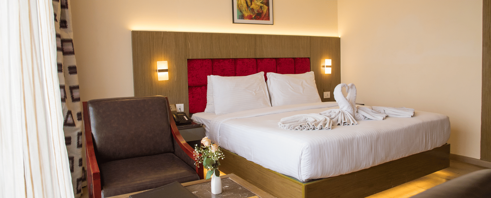 Side angle view of a double bed in a brightly lit Deluxe Room with a back lit headboard at the Benzz Park, Vellore.