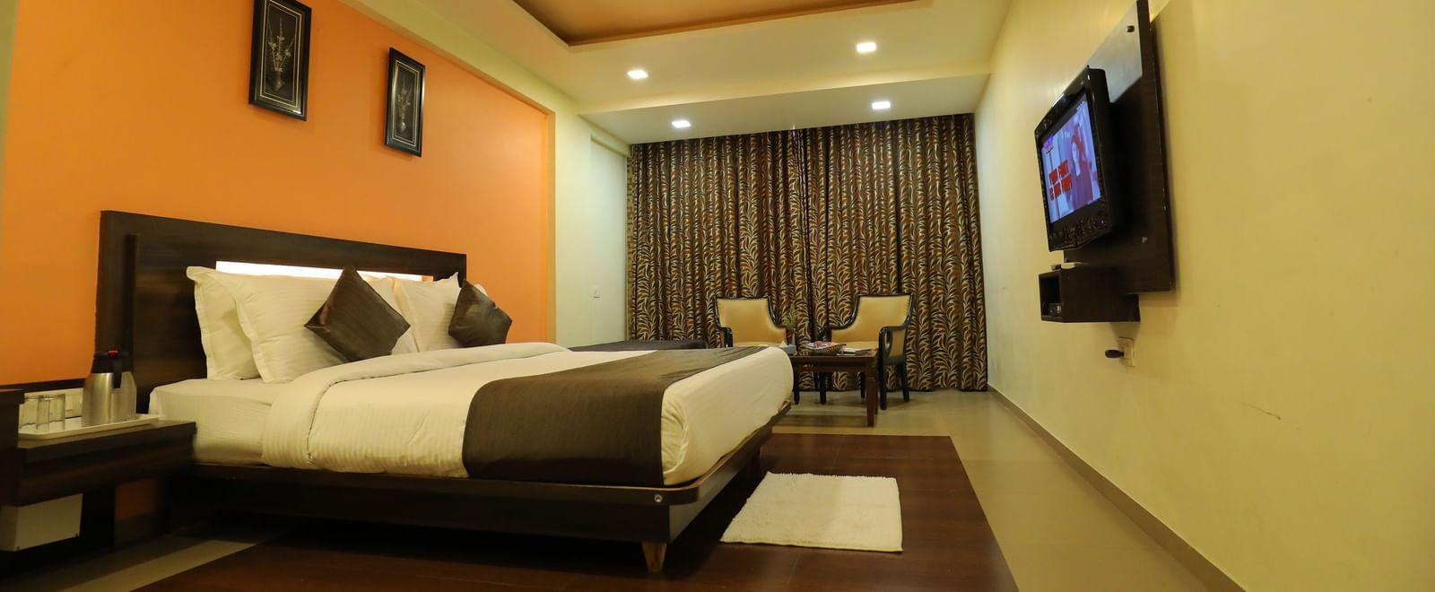A spacious bedroom at Krushnai Resort with a bed, an orange wall, and a large TV mounted on the wall.