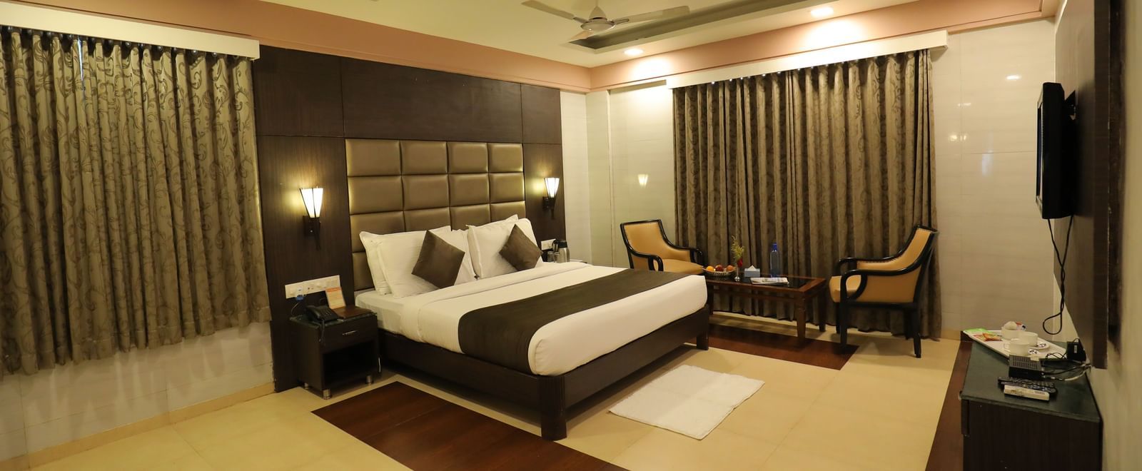 A front angle view of a bedroom at Krushnai Resort with a king size bed, a dark headboard, and brown drapes.