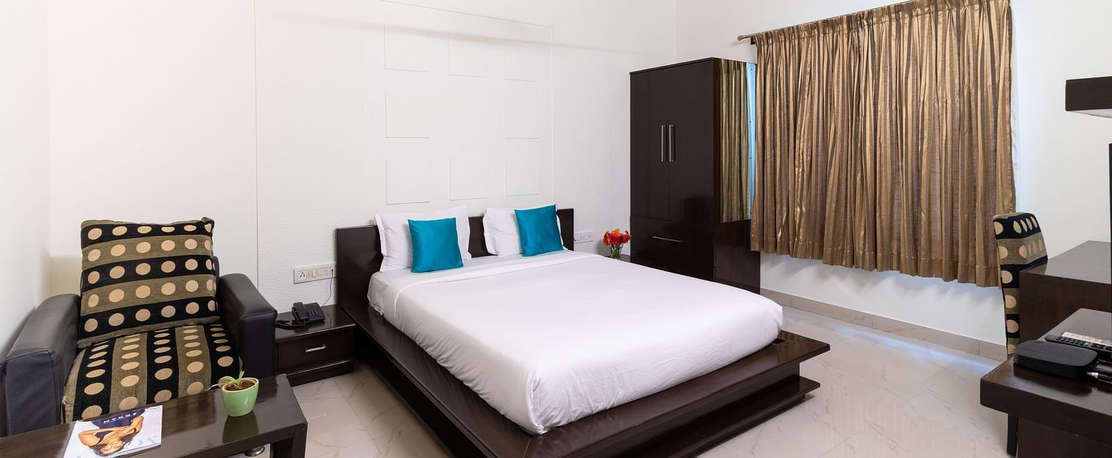 A tidy bedroom with a double bed, a sofa, and a white ceiling fan at Sanctum Suites Domlur, Bangalore.