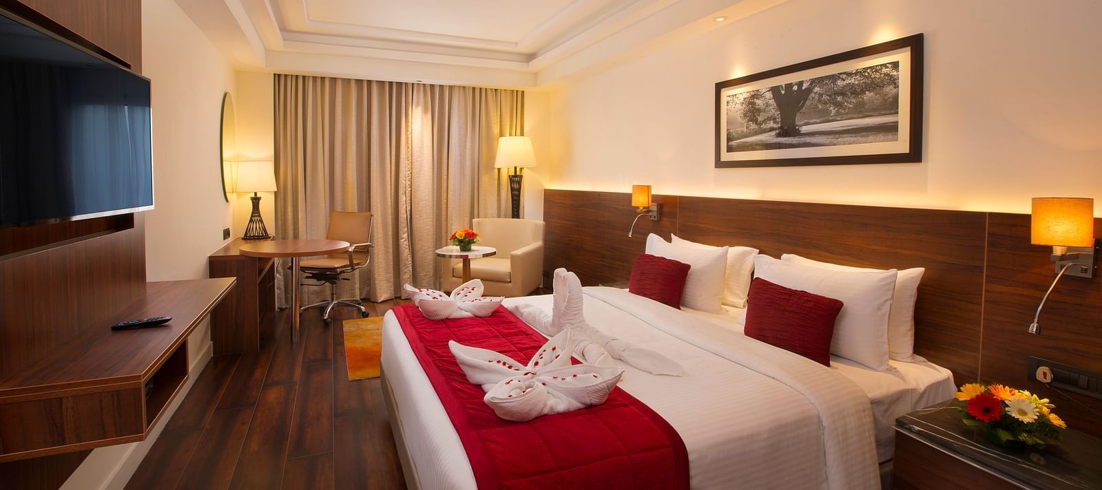 An elegant hotel room with a large bed, red throw blanket, decorative pillows and a framed black-and-white photograph on the wall - Hotel Southend by TGI - Bommasandra, Bangalore