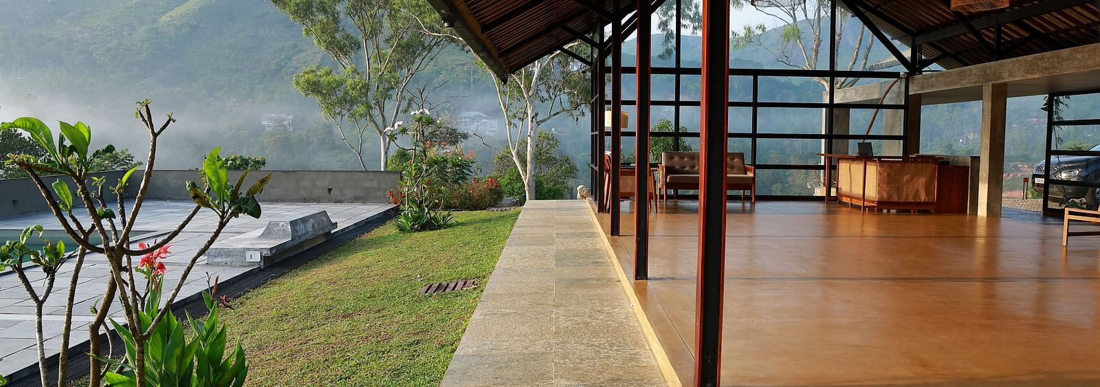  A spacious open-air pavilion at Vaastha Vagamon, featuring an exposed roof structure and offering panoramic views of the surrounding hills.