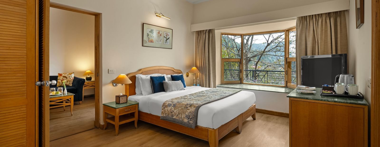 Superior Cottage Hill View bedroom featuring a double bed, a balcony, a table with tea amenities, a mirror, and a wardrobe on the side, with a photo frame hanging above the bed -  Baikunth resort, kasauli 